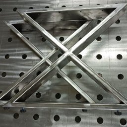 A.I.M Weld Usługi Spawalnicze MARIUSZ PARUZEL - Metalowa konstrukcja spawana z profili, tworząca geometryczny wzór na perforowanym stole spawalniczym. Widoczne ślady obróbki i spawania.