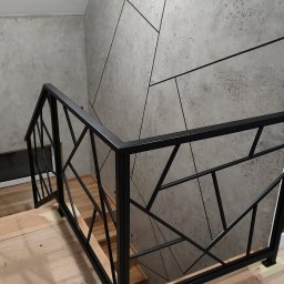 A.I.M Weld Usługi Spawalnicze MARIUSZ PARUZEL - Nowoczesna, czarna balustrada schodowa z geometrycznym wzorem na tle ściany z efektem betonu. Widoczne drewniane stopnie i zabezpieczenia podłogi.