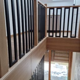 A.I.M Weld Usługi Spawalnicze MARIUSZ PARUZEL - Nowoczesna balustrada schodowa z czarnymi, pionowymi elementami i drewnianymi słupkami, widok z góry, jasne wnętrze z oknem w tle.