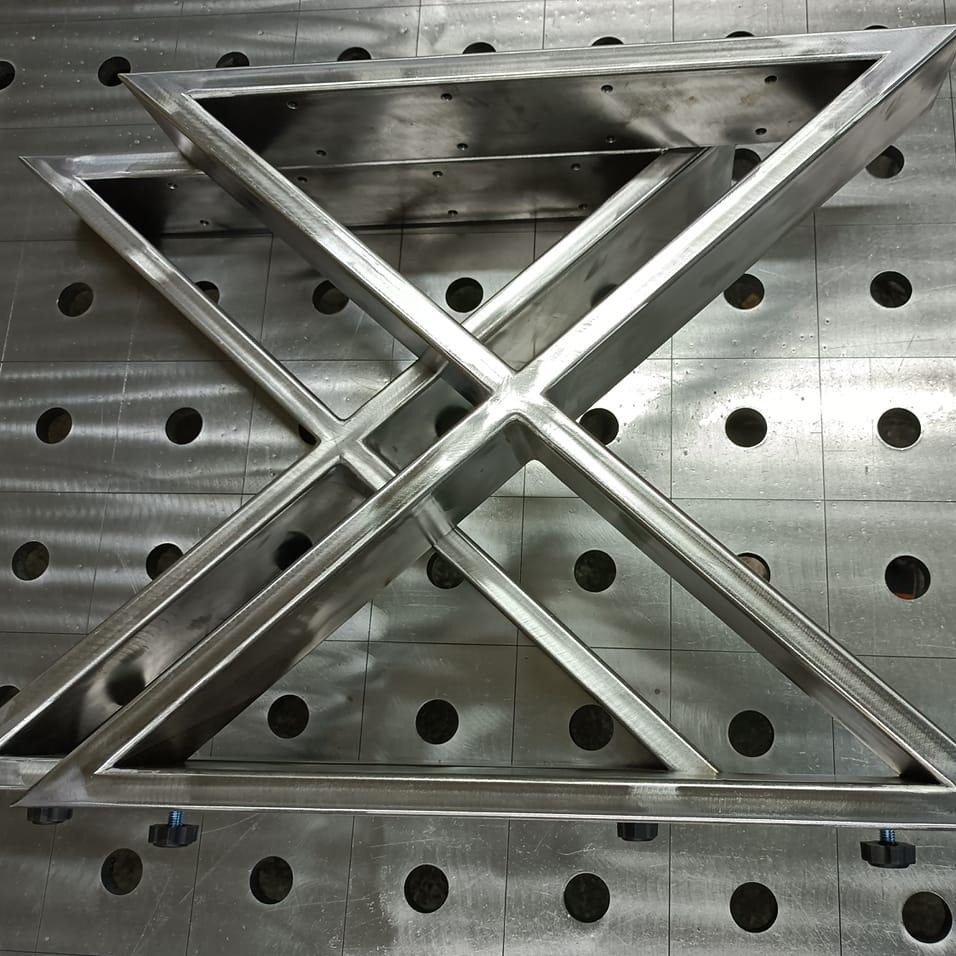 Metalowa konstrukcja spawana z profili, tworząca geometryczny wzór na perforowanym stole spawalniczym. Widoczne ślady obróbki i spawania.