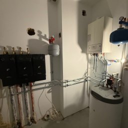 Damir Khassan - Nowoczesna kotłownia z trzema czarnymi modułami, białym piecem gazowym i zbiornikiem. Widoczne rury i instalacje. Ściany białe, surowe wykończenie.