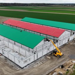 INHOL CONSTRUCTION SPÓŁKA Z OGRANICZONĄ ODPOWIEDZIALNOŚCIĄ - Budowa trzech równoległych hal: dwie z zielonymi, jedna z czerwonym dachem. Na pierwszym planie budynek w stanie surowym otwartym, obok żółta ładowarka teleskopowa z koszem.