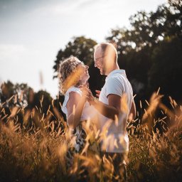 Michał Drewnicki FilmPR - Zakochana para w okularach, w objęciach na tle łąki i drzew, w ciepłym świetle. Uśmiechnięci, w białych koszulkach, romantyczna sesja w plenerze.