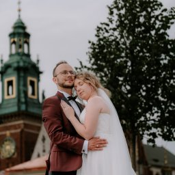 Michał Drewnicki FilmPR - Para młoda w objęciach na tle Wawelu. Pan młody w bordowym smokingu, panna młoda w białej sukni. Romantyczna sesja ślubna w Krakowie.