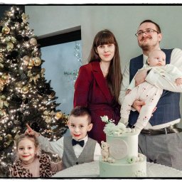 Michał Drewnicki FilmPR - Rodzinne zdjęcie z okazji chrztu, z tortem i choinką. Uśmiechnięci rodzice z dziećmi pozują w świątecznej atmosferze. Na pierwszym planie tort z datą chrztu.
