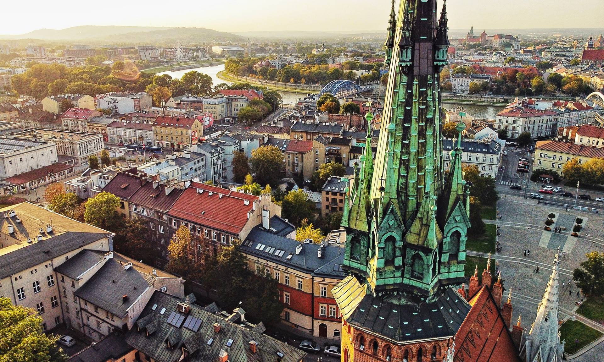 Panorama Krakowa z lotu ptaka, z wieżą kościoła na pierwszym planie. Widok na Stare Miasto, Wisłę i Wawel w oddali, w ciepłym świetle słonecznym.