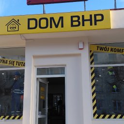 DOM BHP JULIA FILICZKOWSKA - Fasada sklepu Dom BHP z manekinem w odzieży roboczej w oknie. Widoczny szyld z logo i otwarte drzwi wejściowe. Błękitne niebo w tle.