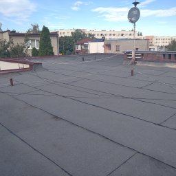 MBud Michał Naciskała - Płaski dach pokryty papą termozgrzewalną, widoczne kominy i instalacje antenowe na tle zabudowy miejskiej w słoneczny dzień. Charakterystyczne łączenia papy.