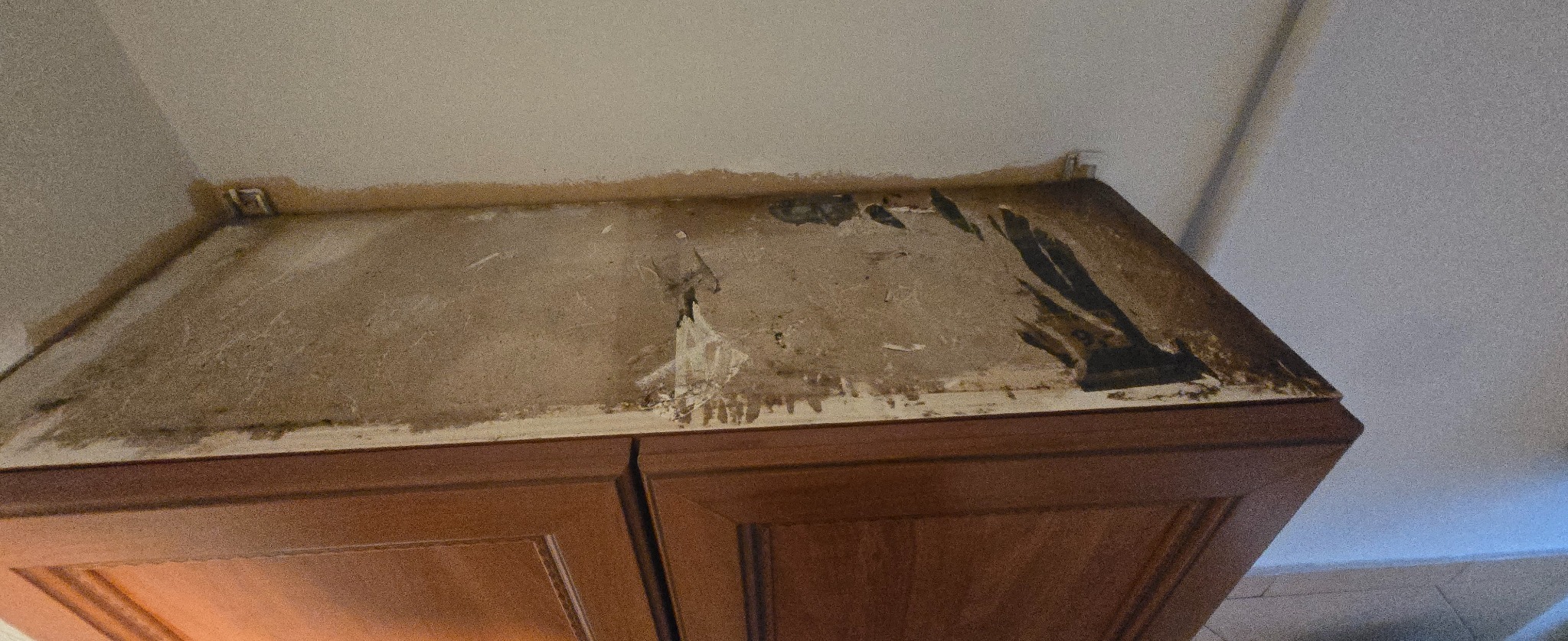 Zabrudzona górna powierzchnia szafki kuchennej, widoczne plamy i zacieki, prawdopodobnie tłuszcz i kurz. Ujęcie z dołu, blisko ściany.