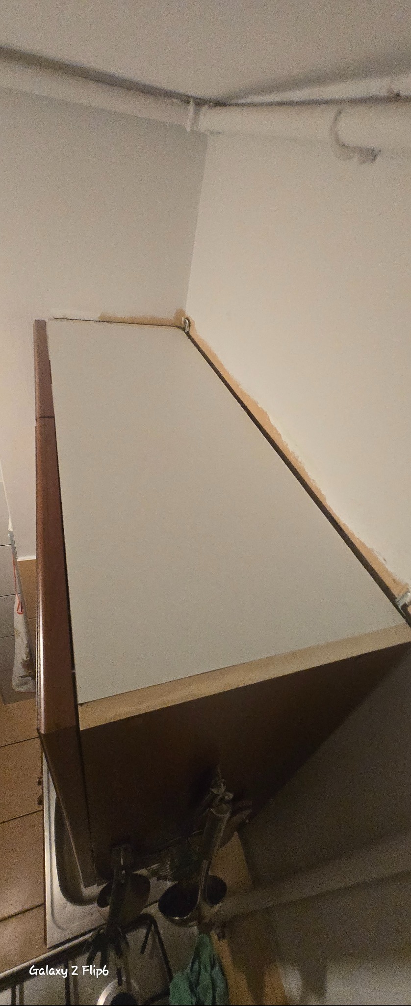 Zamontowana szafka kuchenna z widocznymi elementami instalacji pod zlewem, sfotografowana pod kątem. Widoczne rury i fragment zlewu. Ściana w tle.