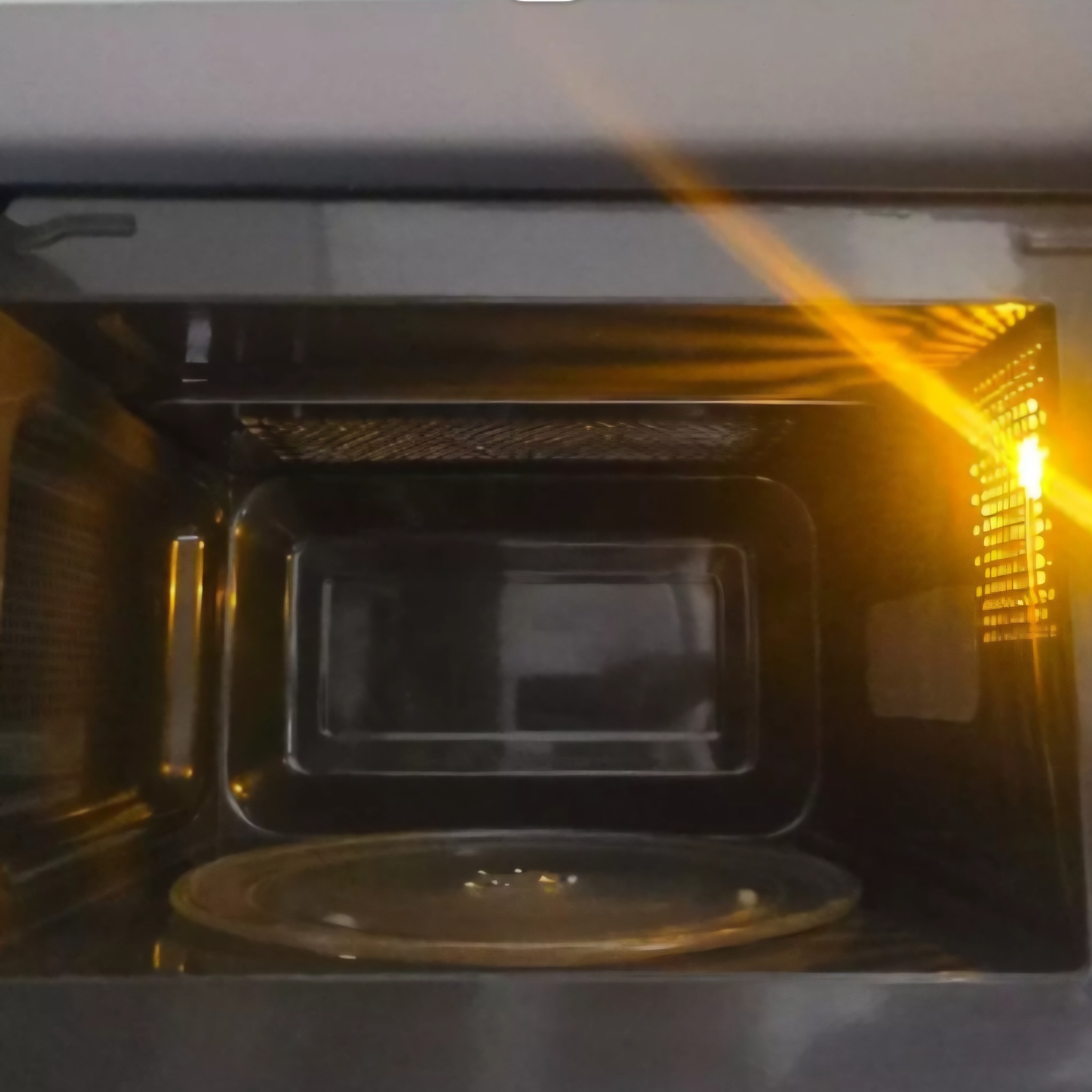 Wnętrze kuchenki mikrofalowej z oświetleniem, widoczny szklany talerz obrotowy. Perspektywa z bliska, wnętrze ciemne, oświetlone z prawej strony.