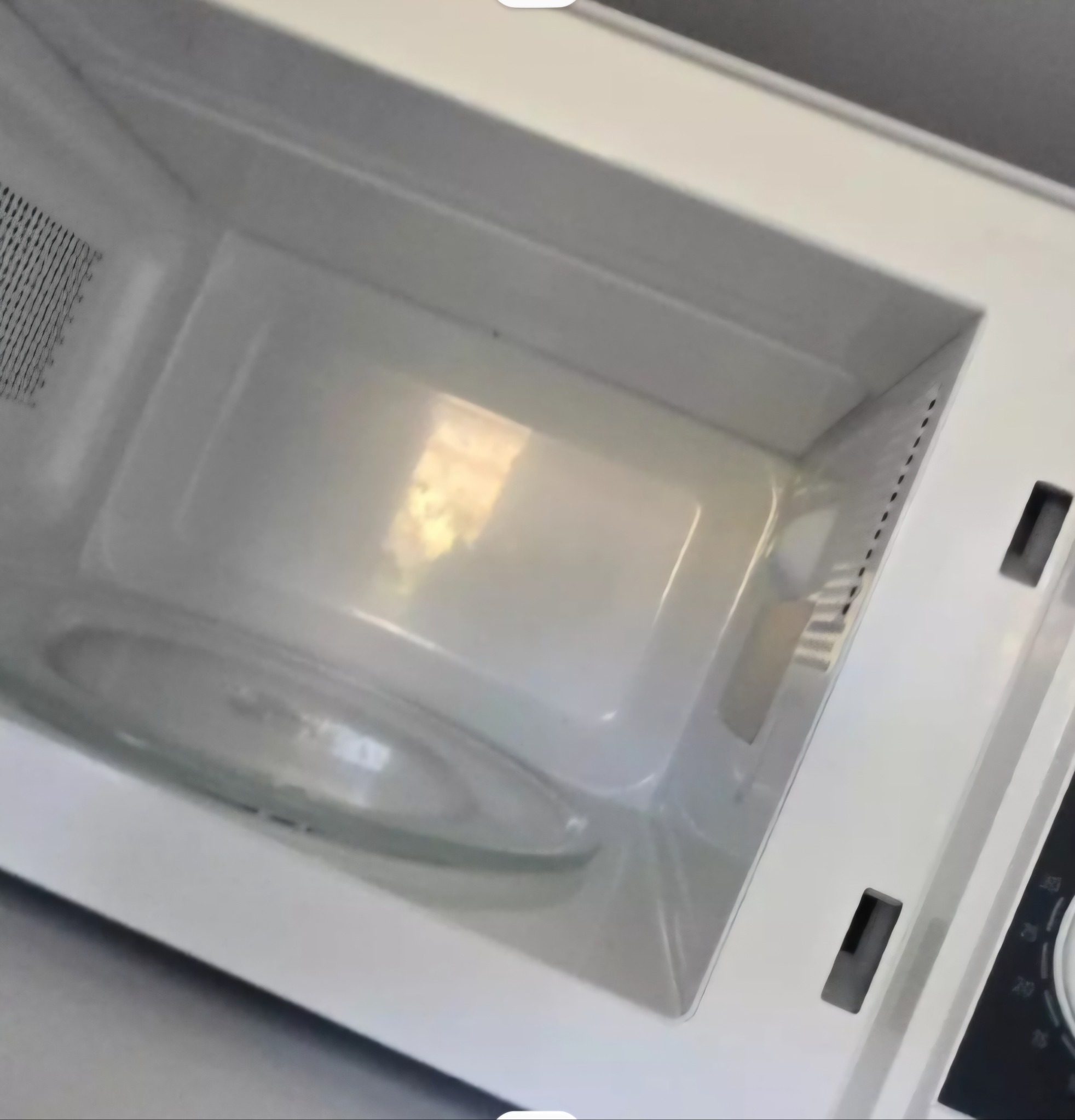 Wnętrze czystej, białej kuchenki mikrofalowej z obrotowym talerzem. Widoczne detale konstrukcyjne i otwory wentylacyjne. Ujęcie z bliska, ukazujące higienę urządzenia.