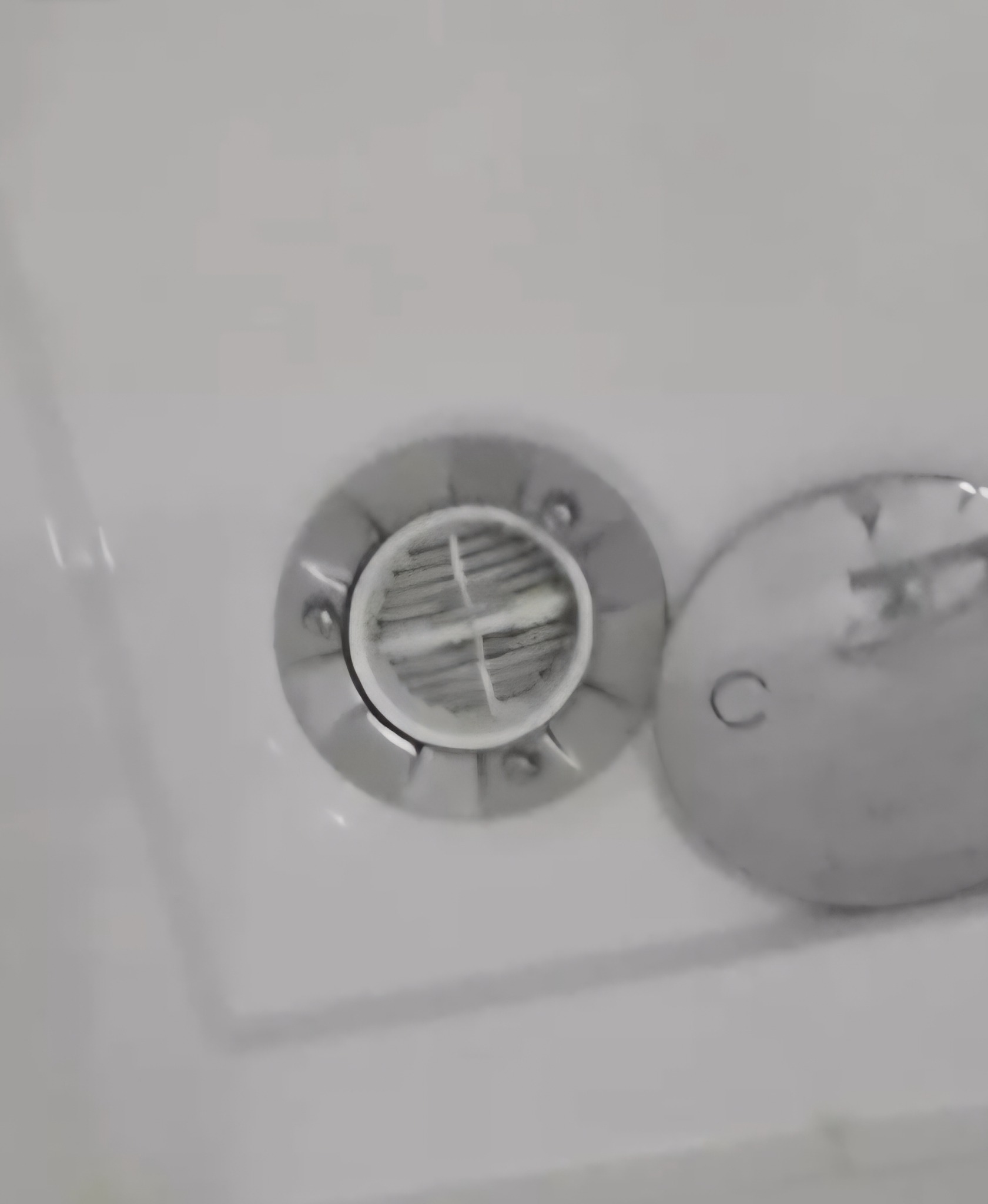 Zablokowany odpływ w brodziku kabiny prysznicowej, zatkany włosami i brudem. Widoczny srebrny korek obok odpływu. Biała powierzchnia brodzika.