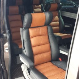 DPIVP SPÓŁKA Z OGRANICZONĄ ODPOWIEDZIALNOŚCIĄ - Wnętrze luksusowego busa z brązowo-czarnymi, skórzanymi fotelami z zagłówkami i podłokietnikami. Widok z otwartych drzwi na przestronne wnętrze pojazdu.