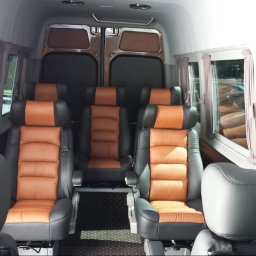 DPIVP SPÓŁKA Z OGRANICZONĄ ODPOWIEDZIALNOŚCIĄ - Wnętrze luksusowego busa z brązowo-czarnymi skórzanymi fotelami, zasłonkami w oknach i dywanikiem w gwiazdki. Widok z perspektywy pasażera.