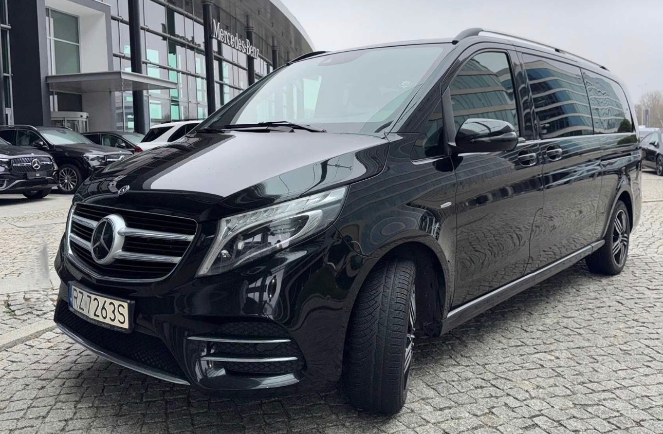 Elegancki, czarny Mercedes-Benz V-klasa z numerem rejestracyjnym RZ 7263S, zaparkowany przed salonem Mercedes-Benz. Widoczne odbicia budynków w szybach.