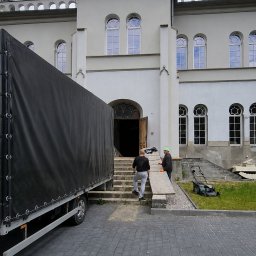 WenaBud - Przeprowadzka do zabytkowego budynku: pracownicy wnoszą zabezpieczenia po schodach, obok zaparkowany bus z plandeką i kosiarka. Nietypowa lokalizacja przeprowadzki.