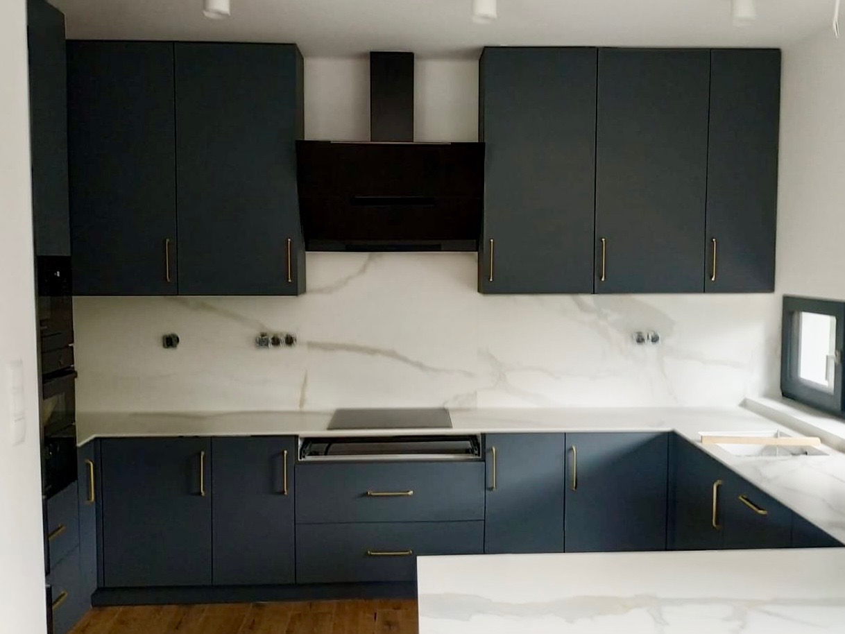 Nowoczesna, grafitowa zabudowa kuchenna z marmurowym blatem i złotymi uchwytami, zrealizowana w Lublinie. Minimalistyczny design, widok na płytę indukcyjną.