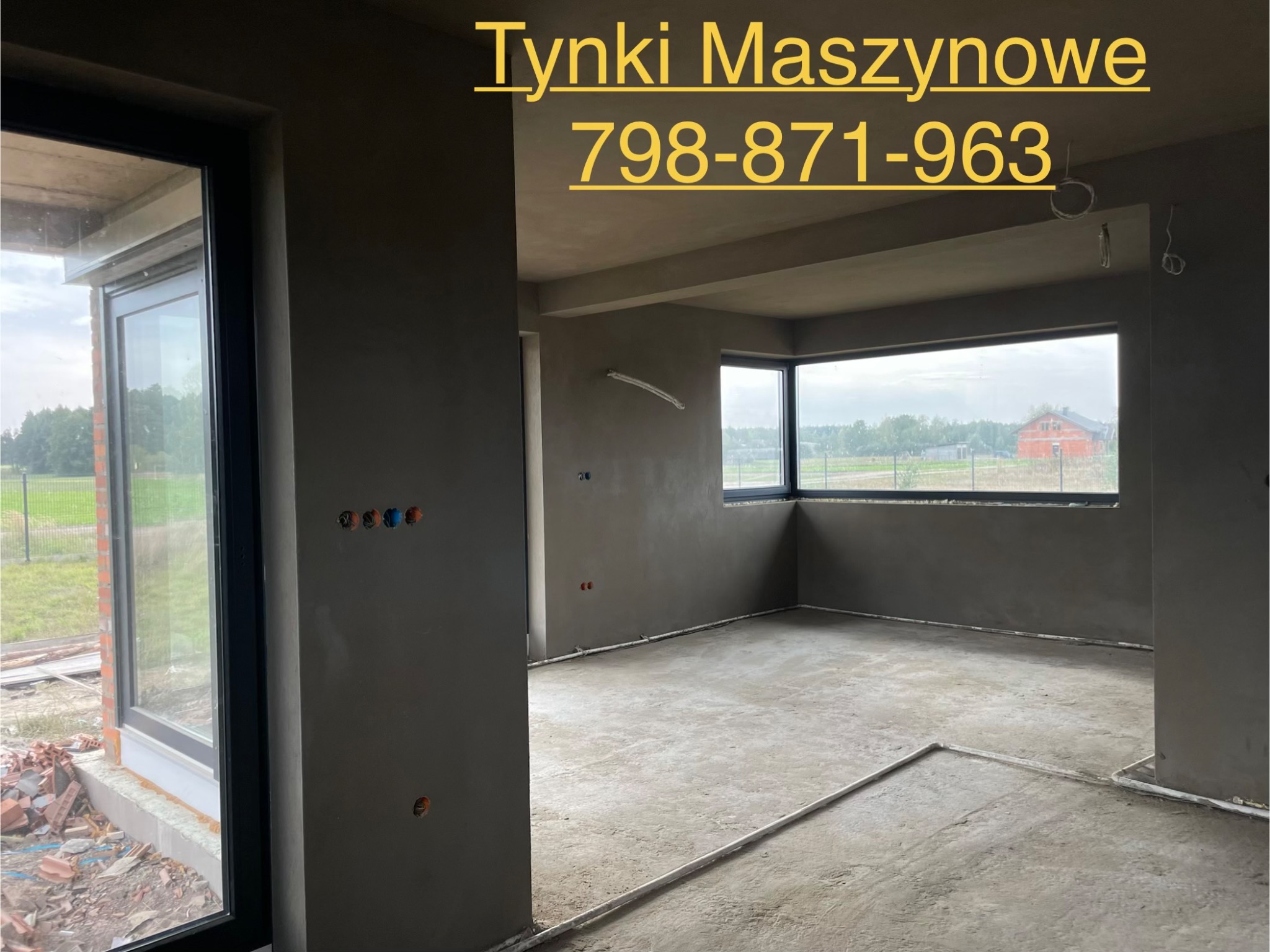 Surowe wnętrze po tynkowaniu maszynowym: szare ściany, okna z widokiem na zieleń, widoczne instalacje elektryczne. Podłoga betonowa, przygotowana do dalszych prac.