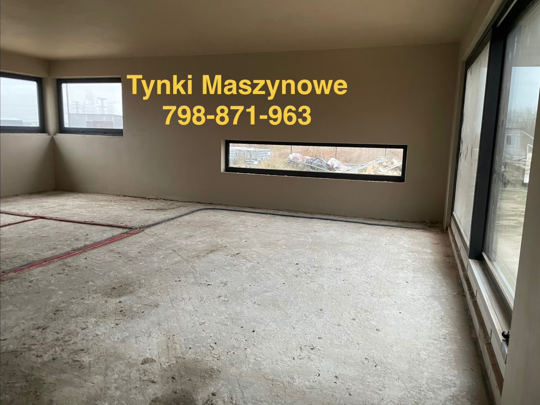 Wnętrze po tynkowaniu maszynowym, widoczne gładkie ściany i instalacja podłogowa. Na ścianie numer telefonu do wykonawcy.