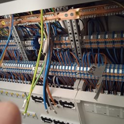 Sylwester Kopiński ElektroVolt-SK Usługi Elektryczne - Rozdzielnia elektryczna z licznymi przewodami w kolorach: niebieskim, brązowym, zielono-żółtym. Widoczne szyny PE i N. Elementy metalowe i plastikowe.