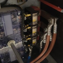 Sylwester Kopiński ElektroVolt-SK Usługi Elektryczne - Rozdzielnica elektryczna z bezpiecznikiem topikowym, wyłącznikiem i przewodami w brązowej obudowie. Widoczne złącza i elementy instalacji.