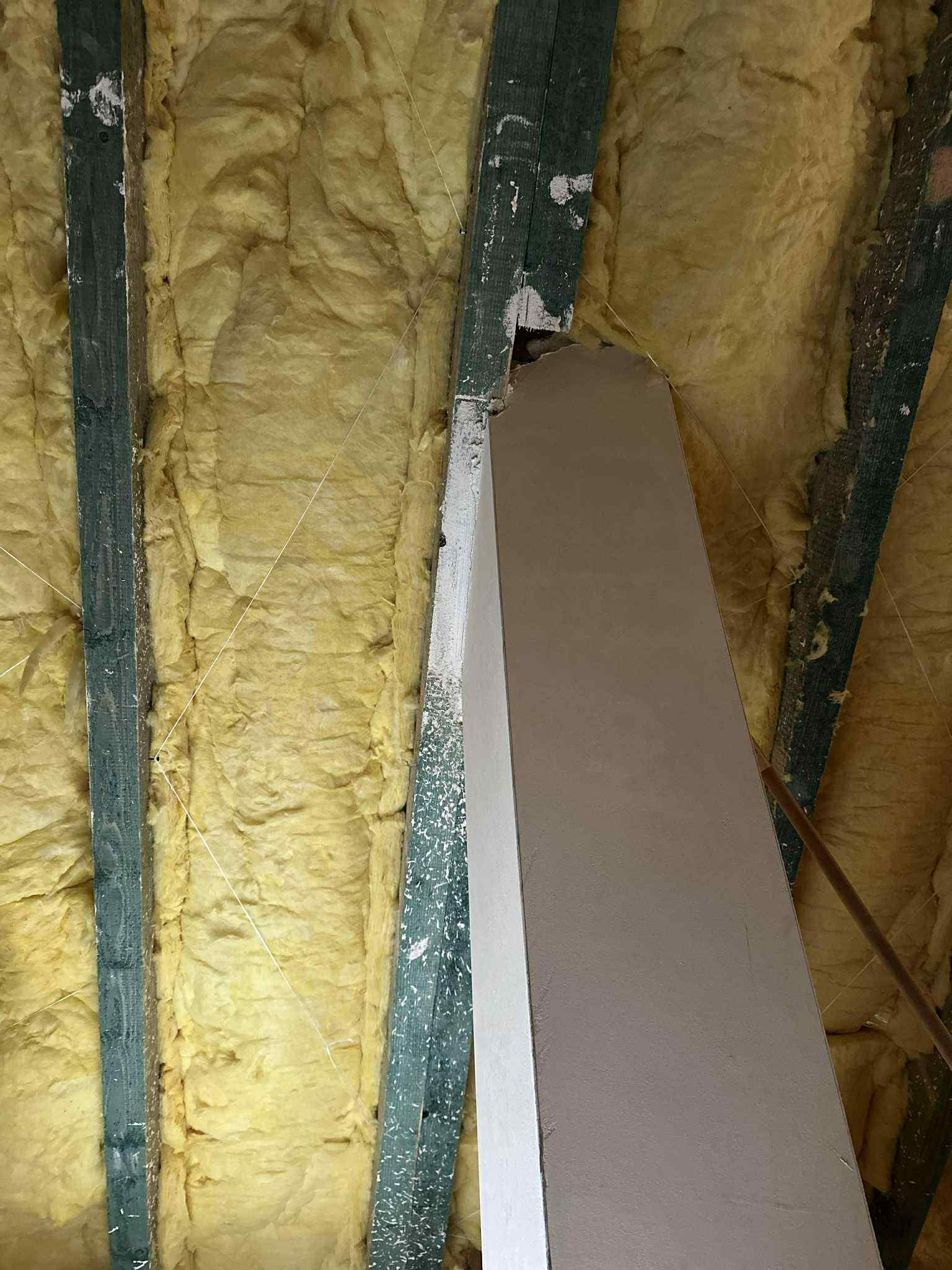 Ocieplone wełną mineralną poddasze z drewnianą konstrukcją i fragmentem obudowanego komina. Widoczne białe ślady po obróbce gipsowej.