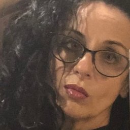 Usługi projektowe, Nieruchomości. Bożena Zyznawska - Portret kobiety w okularach z ciemnymi kręconymi włosami, ujęcie z bliska, z widocznym odbiciem w okularach. Delikatny makijaż, błyszczące usta.