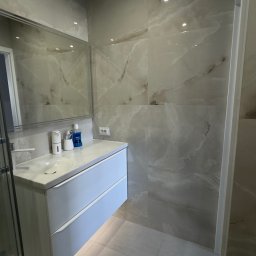 Fast Bilding Vasyl Voloshyn - Nowoczesna łazienka z marmurowymi płytkami, podwieszaną szafką z umywalką i lustrem. Minimalistyczny design, jasne kolory i subtelne oświetlenie.