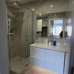 Fast Bilding Vasyl Voloshyn - Nowoczesna łazienka z kabiną prysznicową, umywalką z szafką i dużym lustrem. Jasne płytki imitujące marmur na ścianach i podłodze. Oświetlenie punktowe.