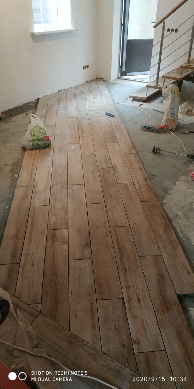 Układanie podłogi z płytek imitujących drewno w trakcie remontu. Widoczne narzędzia i materiały budowlane. Częściowo ułożona podłoga w jasnym pomieszczeniu.