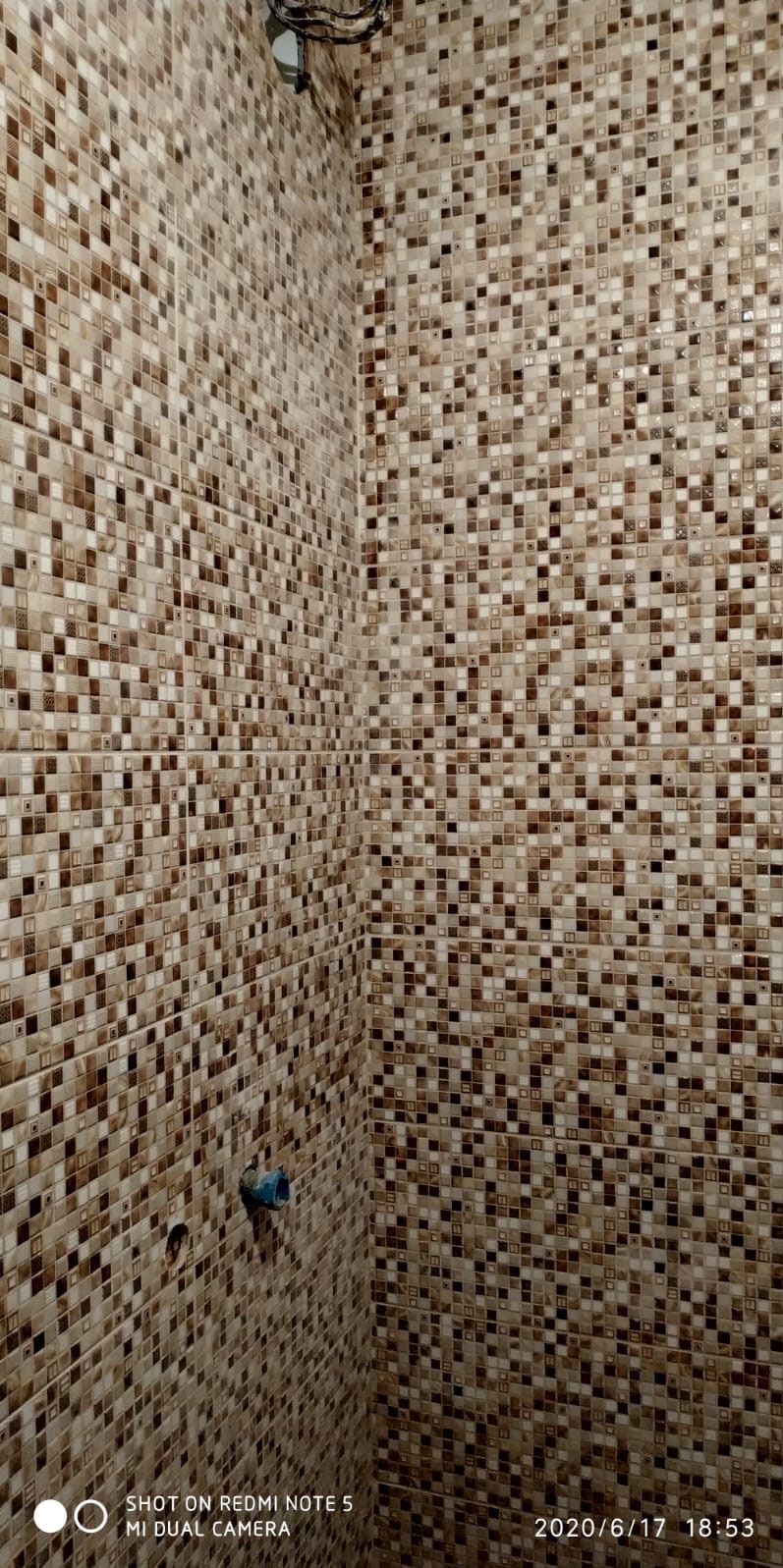 Ściana w łazience wyłożona mozaiką w odcieniach brązu i beżu. Widoczny fragment instalacji wodnej. Ujęcie z dołu, podkreślające fakturę i wzór mozaiki.
