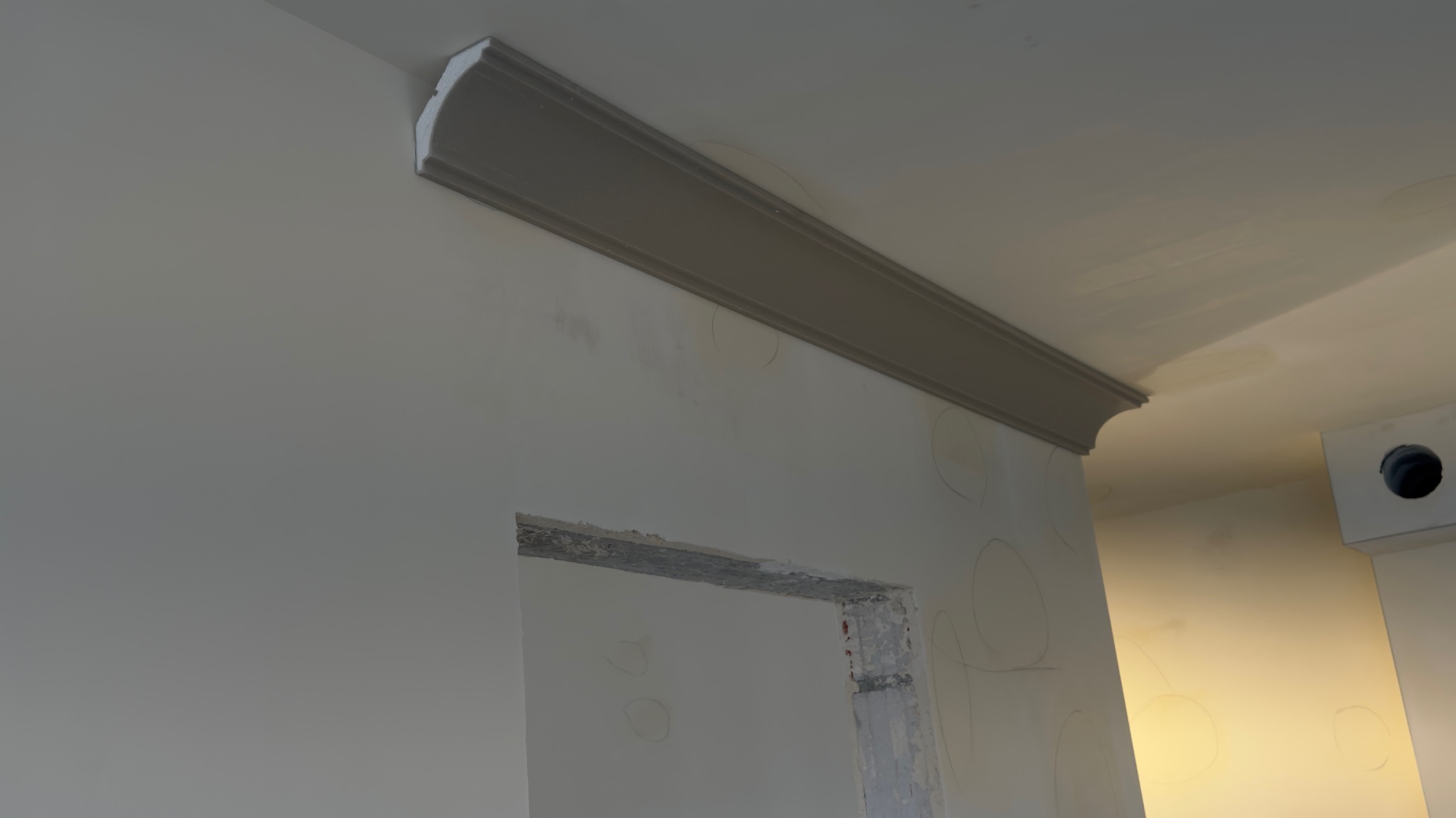 Szara listwa dekoracyjna zamontowana pod sufitem w trakcie prac wykończeniowych. Widoczne ślady po szpachlowaniu i zaznaczone okręgi na ścianie.