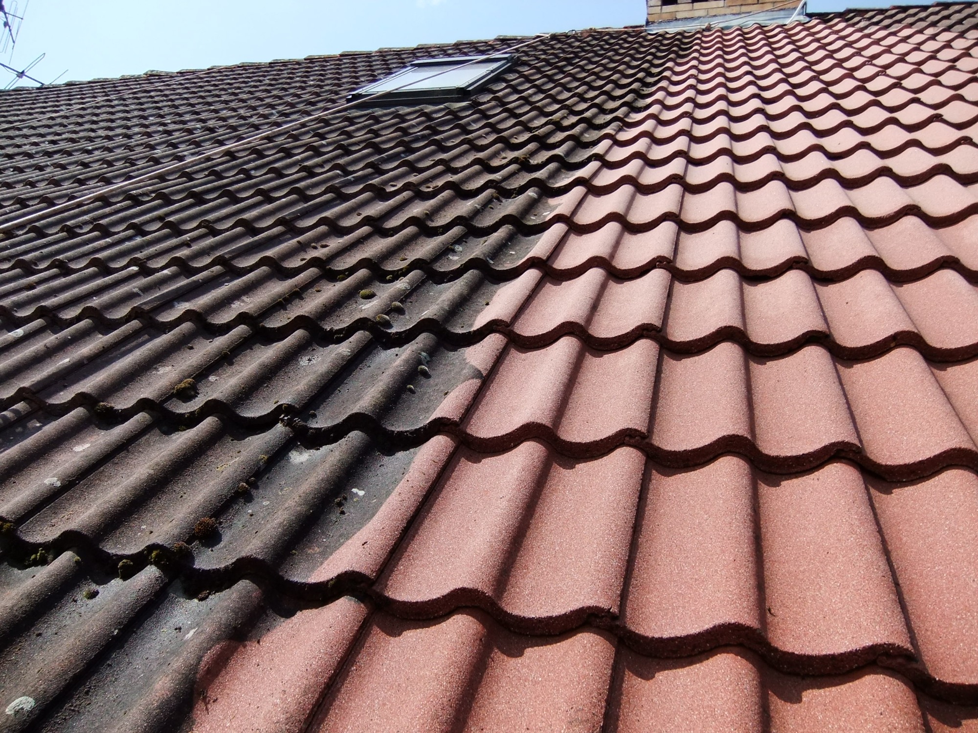 Częściowo wyczyszczony dach z dachówki ceramicznej, widoczna wyraźna różnica między brudną, porośniętą mchem lewą stroną a czystą, czerwoną prawą stroną dachu.