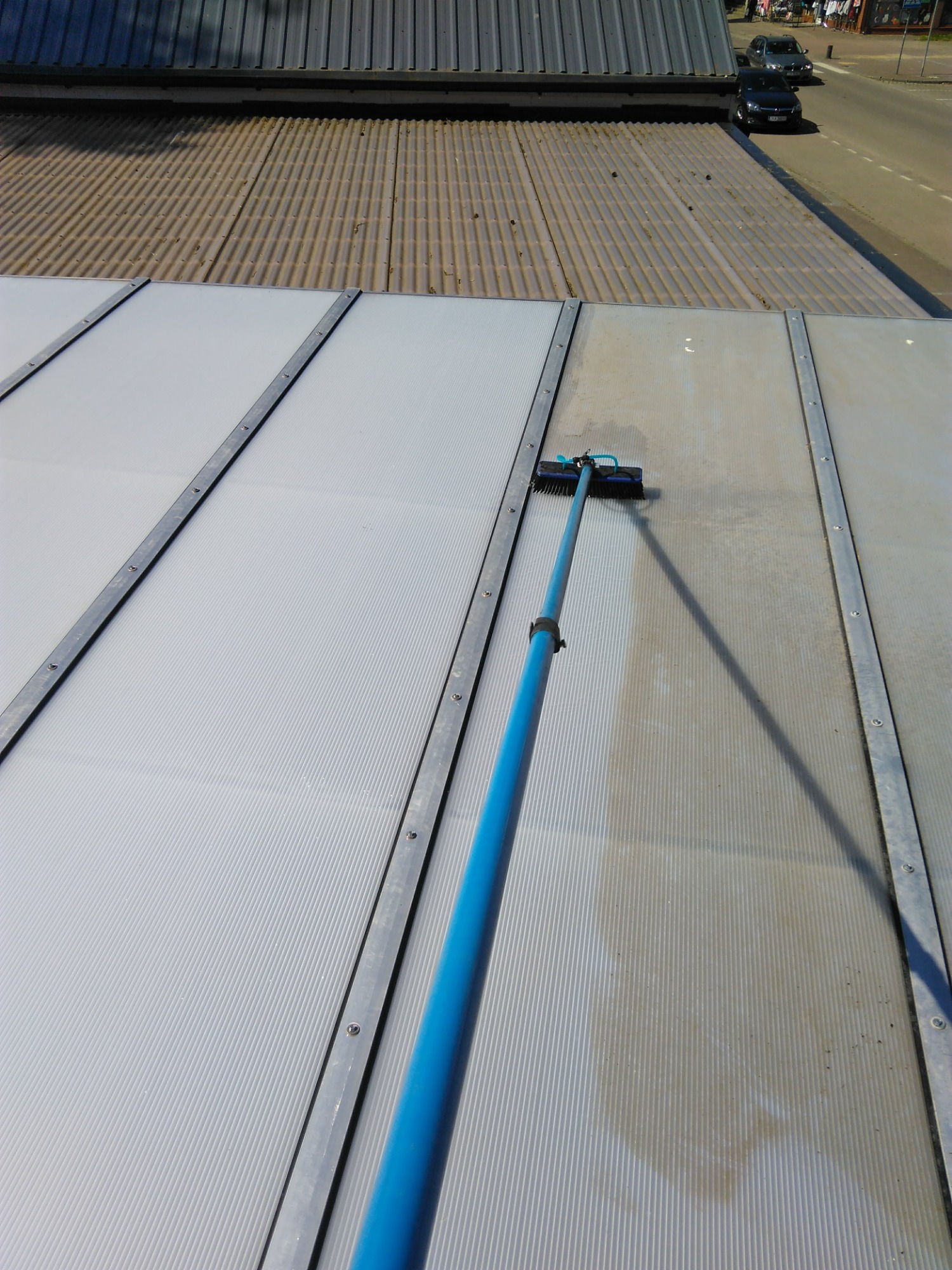 Czyszczenie zadaszenia z pleksi szczotką teleskopową, widoczny efekt przed i po umyciu.