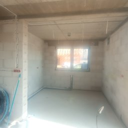 ZWARCIE Mateusz Mioduszewski - Surowy stan: instalacja elektryczna w nowym budynku z widocznymi puszkami i przewodami na ścianach z betonu komórkowego, z rolką zielonego kabla w rogu.