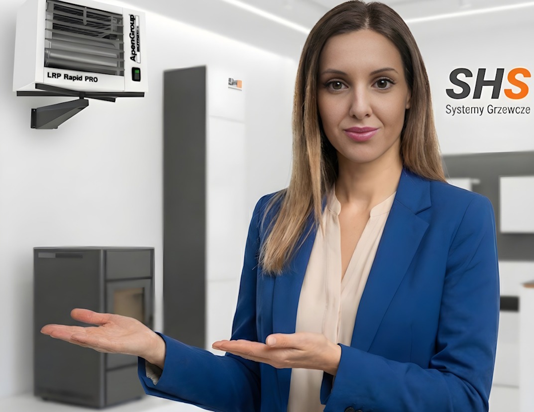 Prezentacja systemów grzewczych SHS: kobieta w niebieskim żakiecie gestykuluje dłońmi, obok grzejnik LRP Rapid PRO i piec wolnostojący na tle minimalistycznego wnętrza.