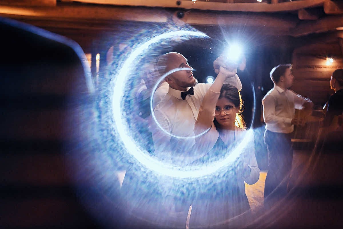 Para podczas tańca otoczona efektem świetlnym w kształcie półksiężyca, uchwycona w dynamicznym ujęciu z lekkim rozmytym tłem i ciepłym oświetleniem.