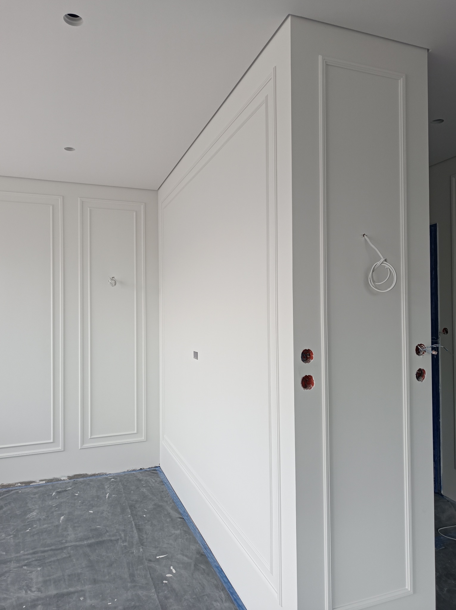 Białe ściany z dekoracyjnymi listwami w stylu klasycznym, zabezpieczona podłoga, gniazdka elektryczne w Warszawie. Detal wykończenia wnętrza.