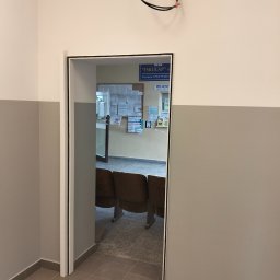 Oleksandr Soboda - Otwór drzwiowy z nową ościeżnicą w pomieszczeniu z szarą lamperią. Widoczny fragment instalacji elektrycznej pod sufitem i wnętrze poczekalni.