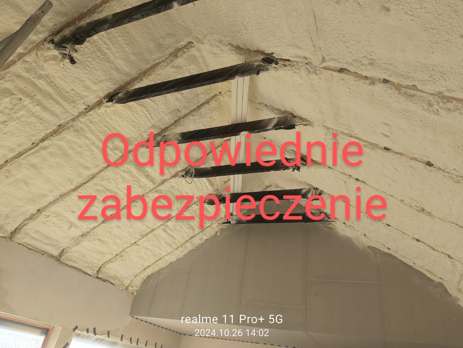 Poddasze po natrysku pianki PUR, widoczne czarne elementy konstrukcyjne dachu. Pianka równomiernie pokrywa powierzchnię, tworząc jednolitą warstwę izolacyjną.