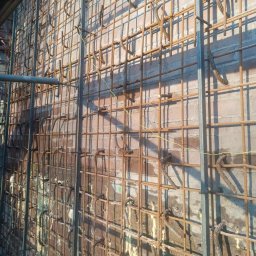 Kamil Chatya - Zbrojenie ściany z cegły z widocznymi elementami stalowymi i pianką montażową. Detal konstrukcji budynku żelbetowego w trakcie budowy, z bliska.