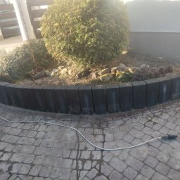 Bruk - Ułożona kostka brukowa na podjeździe, obrzeże z betonowych palisad, tuja. Widoczne ślady wilgoci i kabel zasilający. Praca brukarska w ogrodzie.