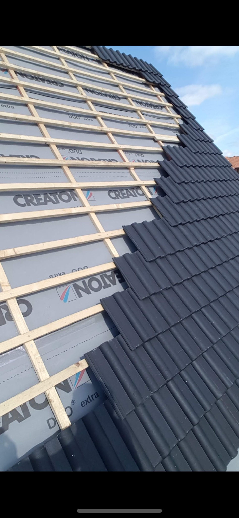 Częściowo pokryty dachówką dach z widoczną membraną CREATON i drewnianą konstrukcją. Układanie dachówki w trakcie realizacji.