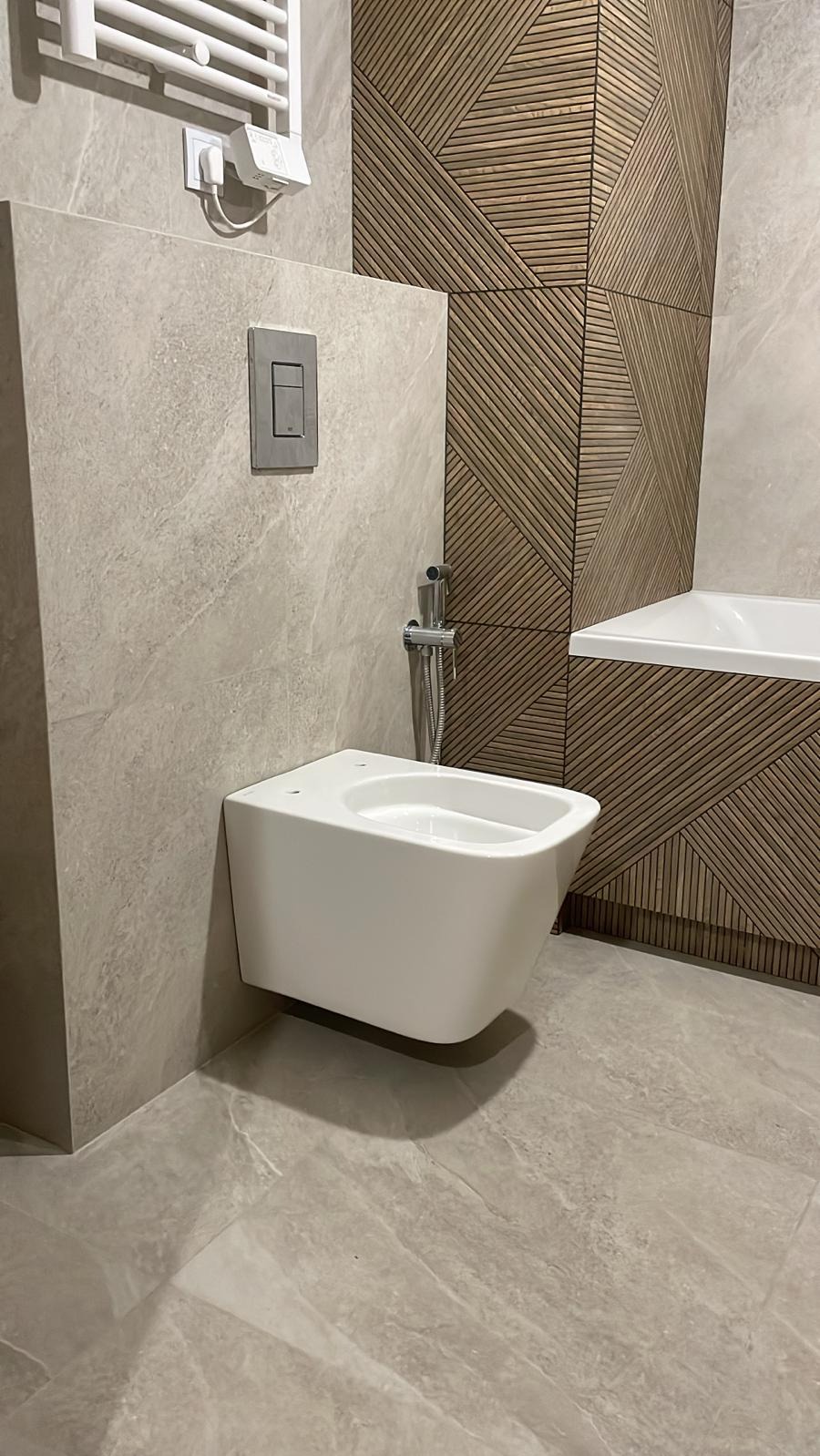 Nowoczesna łazienka z podwieszanym bidetem, płytkami imitującymi marmur i drewnianą mozaiką. Minimalistyczny design, stonowana kolorystyka, eleganckie wykończenie.