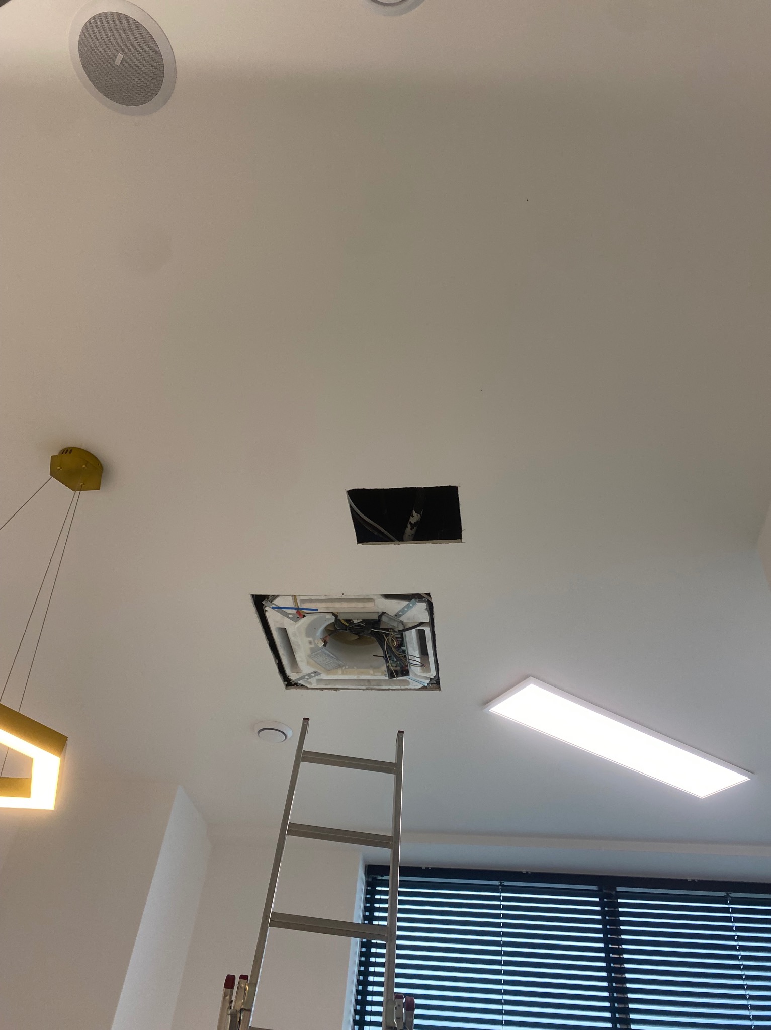 Montaż sufitowej klimatyzacji kasetonowej w pomieszczeniu z oknem. Widoczna drabina, otwór w suficie i częściowo zamontowane urządzenie. Oświetlenie LED.