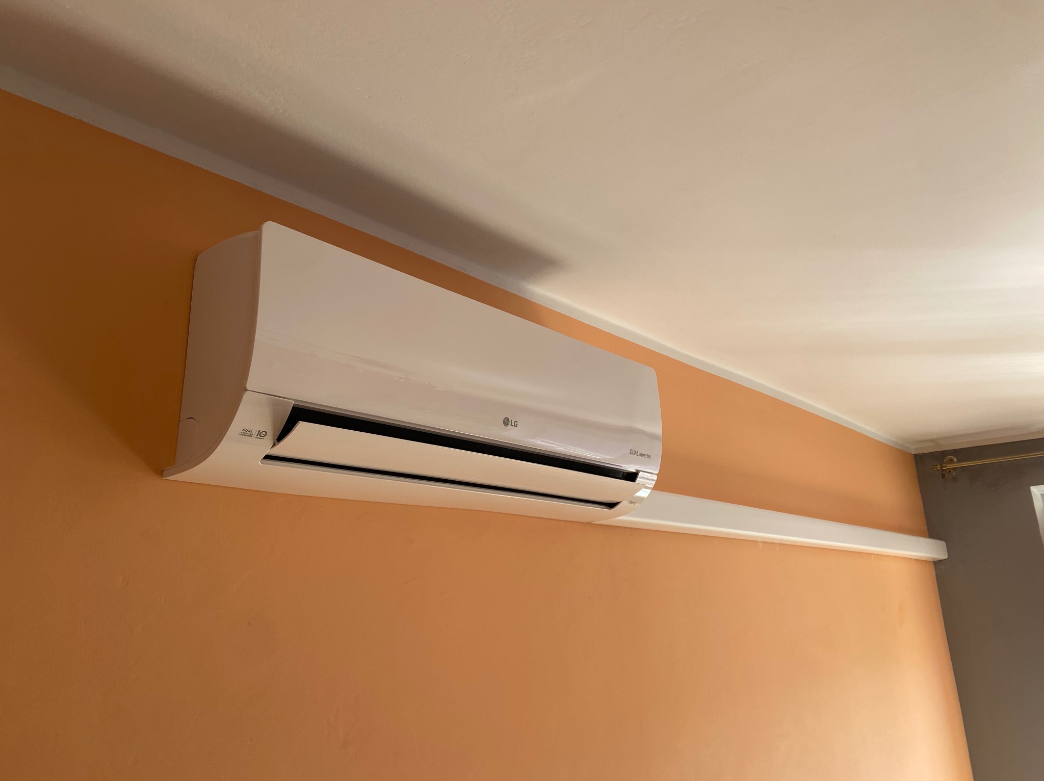 Biały klimatyzator LG Dual Inverter zamontowany na pomarańczowej ścianie w Radunicy. Widok z dołu, lekki kąt. Otwarta klapa nawiewu.