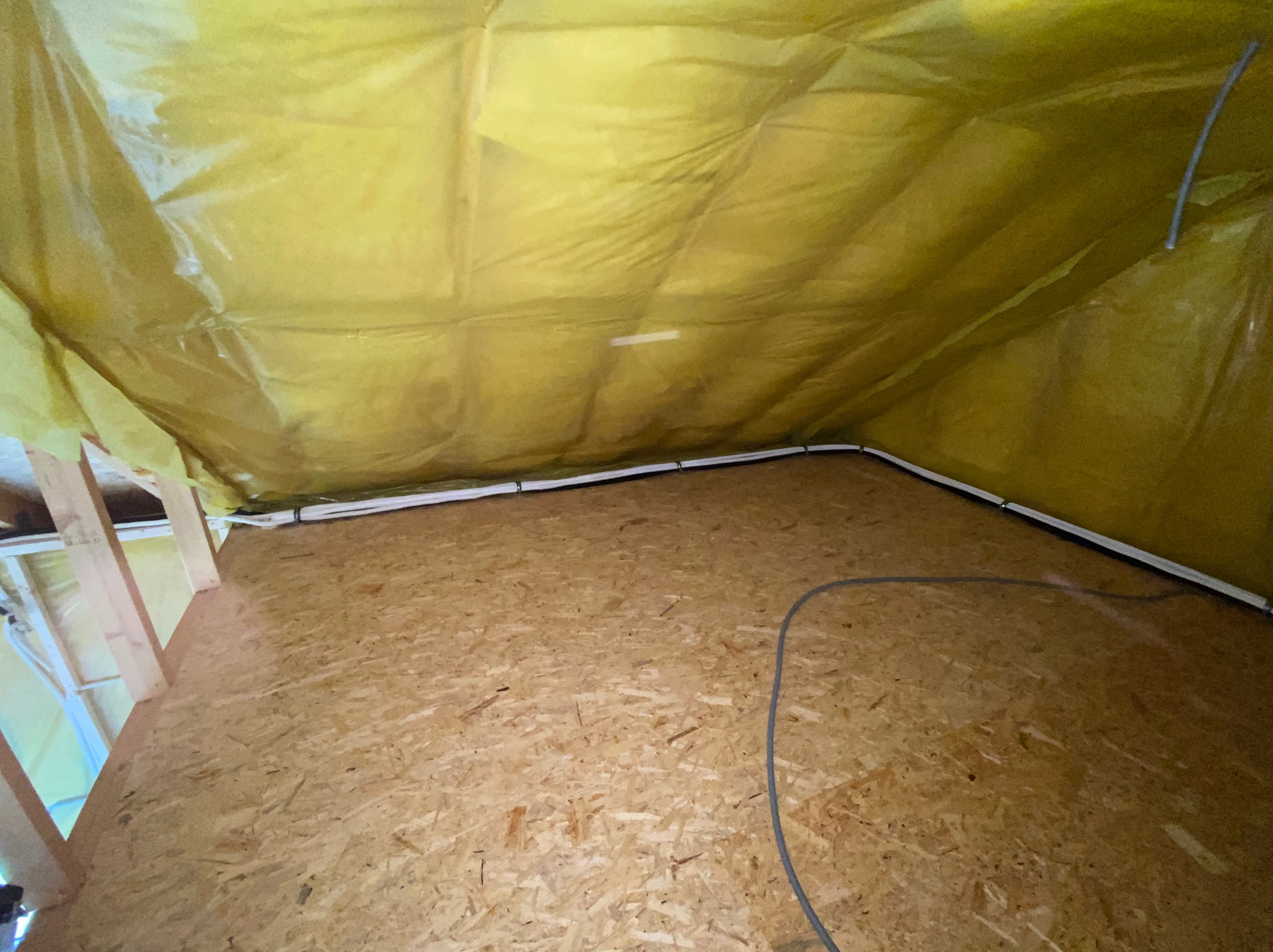 Izolacja poddasza z widocznymi przewodami instalacji, zabezpieczona folią. Ujęcie z dołu, ukazujące strukturę płyty OSB podłogi i drewniane elementy konstrukcyjne.