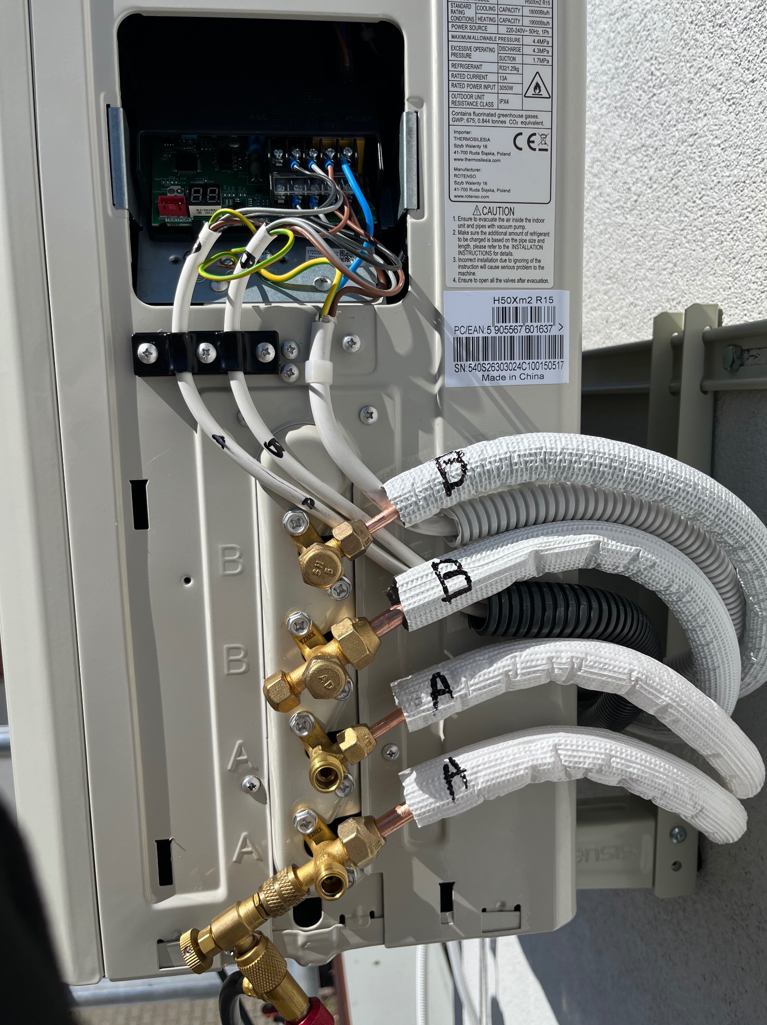 Podłączenie przewodów chłodniczych oznaczonych A i B do zewnętrznej jednostki klimatyzacji. Widoczne zawory i izolowane rury.