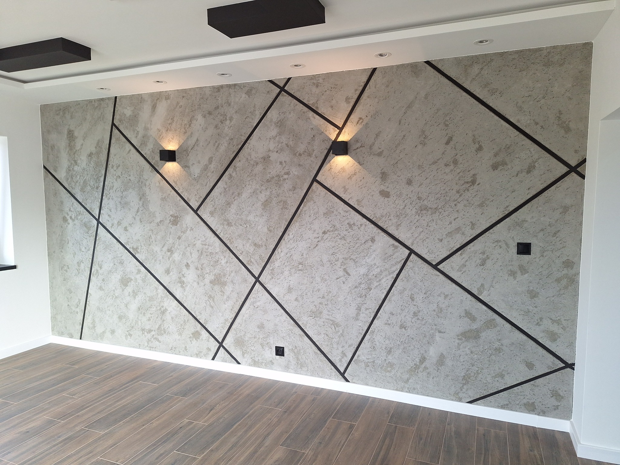 Dekoracyjna ściana z geometrycznym wzorem i oświetleniem punktowym. Podłoga z paneli imitujących drewno. Nowoczesne wykończenie wnętrza z dbałością o detale.